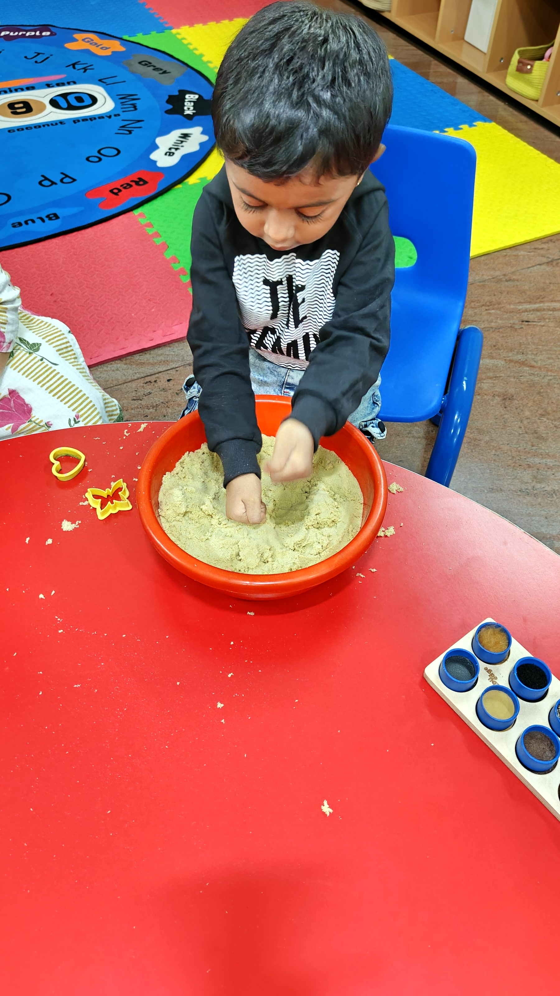 Child practising a fine-motor activity at a red table